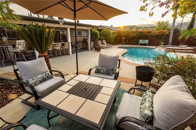 view of swimming pool featuring a patio, fence, outdoor dining area, a pool with connected hot tub, and a grill