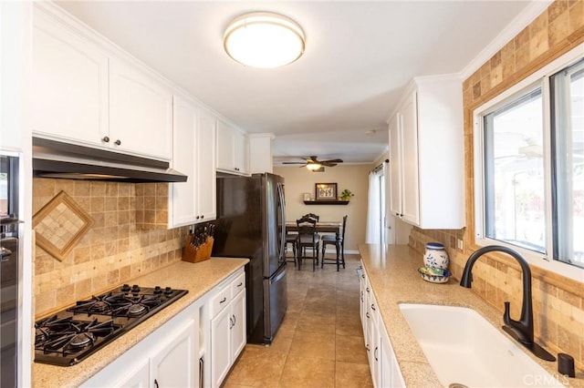 kitchen with under cabinet range hood, black gas cooktop, freestanding refrigerator, white cabinetry, and a sink