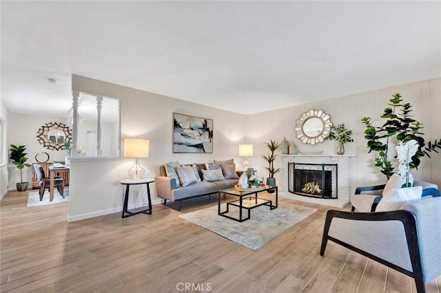 living area with baseboards, a brick fireplace, and light wood-style flooring