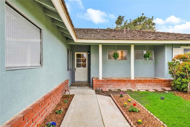 property entrance featuring brick siding, roof with shingles, and stucco siding