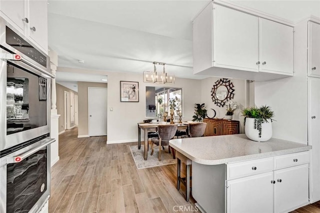 kitchen featuring double oven, white cabinetry, light countertops, and light wood-style floors