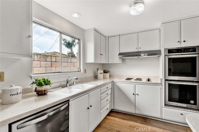 kitchen featuring under cabinet range hood, light wood-type flooring, light countertops, stainless steel appliances, and a sink