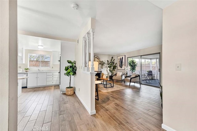 hallway featuring light wood-style flooring, baseboards, and a sink