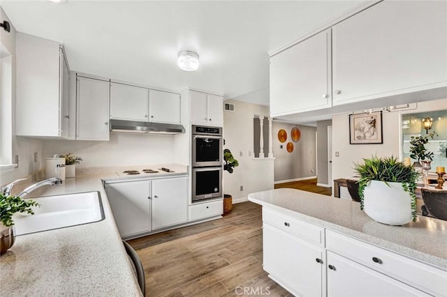 kitchen with double oven, light countertops, under cabinet range hood, and a sink