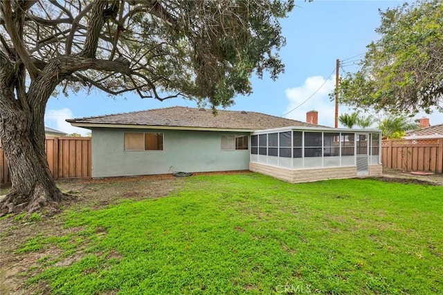 rear view of house featuring a sunroom, stucco siding, a chimney, a yard, and a fenced backyard