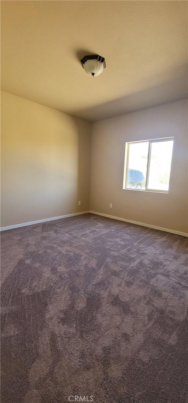 spare room with baseboards and dark colored carpet