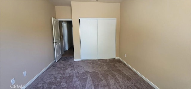 unfurnished bedroom with a closet, baseboards, and dark carpet