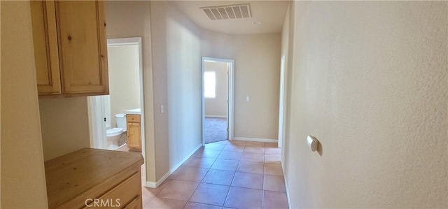 corridor featuring light tile patterned flooring, visible vents, and baseboards