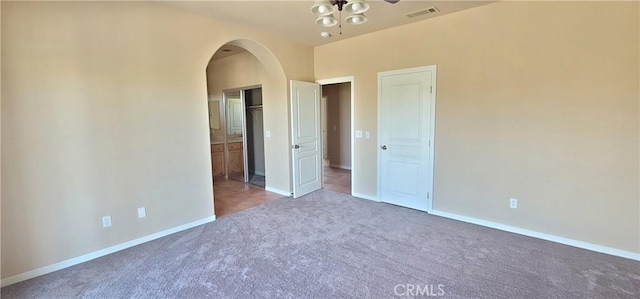 unfurnished bedroom featuring visible vents, arched walkways, carpet, and baseboards