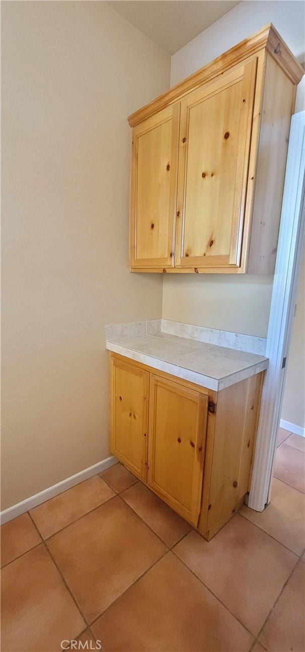 kitchen featuring baseboards, light tile patterned flooring, light brown cabinetry, and light countertops