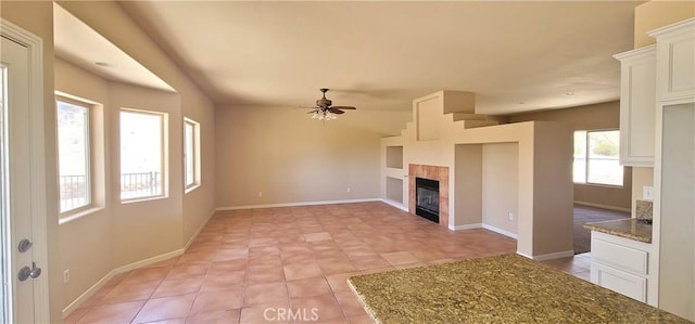 unfurnished living room with a tiled fireplace, a ceiling fan, and baseboards