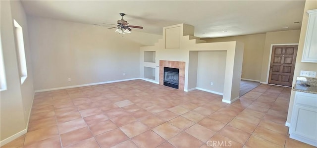 unfurnished living room with a tiled fireplace, baseboards, and a ceiling fan