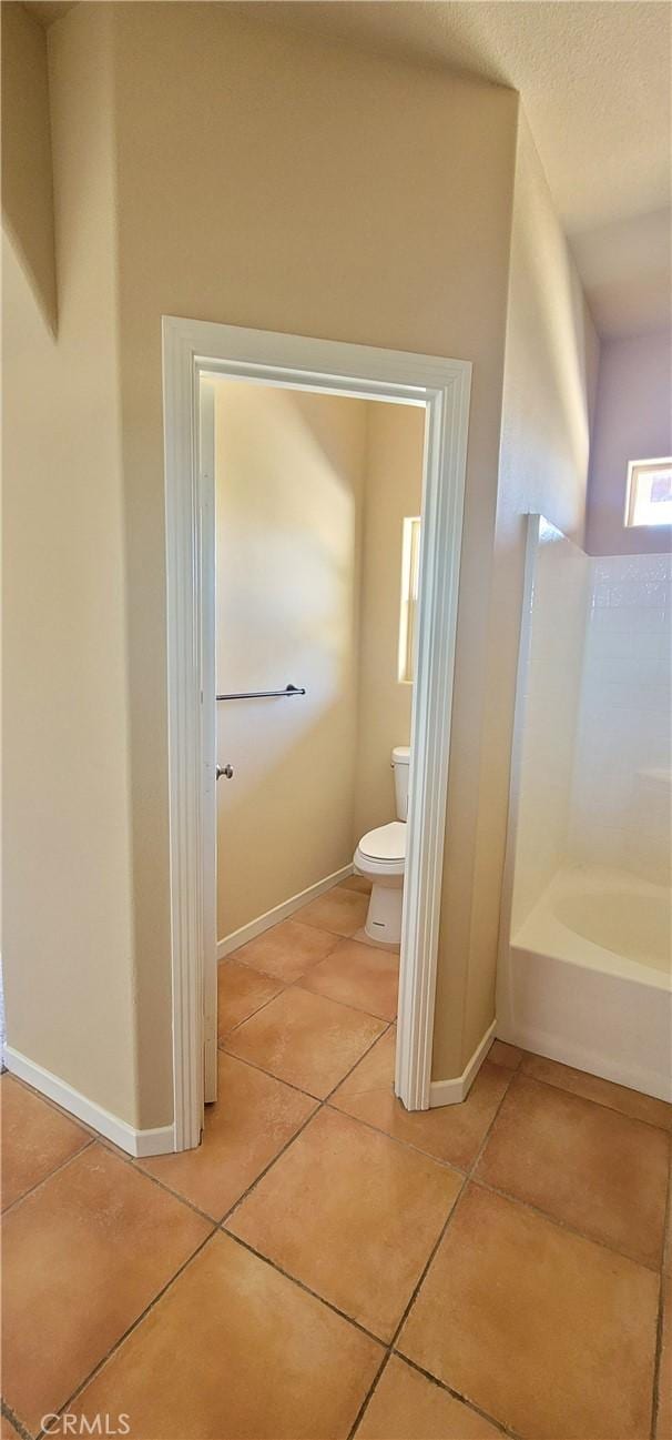 bathroom with baseboards, toilet, a bath, and tile patterned flooring