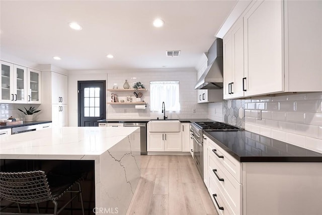 kitchen featuring visible vents, a sink, wall chimney range hood, appliances with stainless steel finishes, and open shelves