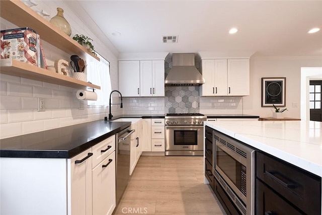 kitchen featuring appliances with stainless steel finishes, plenty of natural light, white cabinets, wall chimney exhaust hood, and a sink