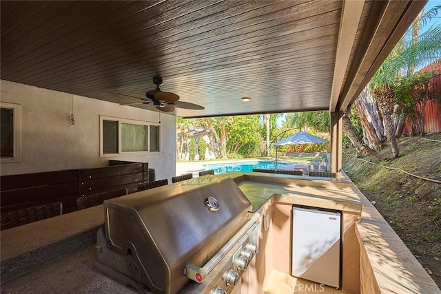 view of patio featuring fence, a ceiling fan, exterior kitchen, an outdoor pool, and a grill