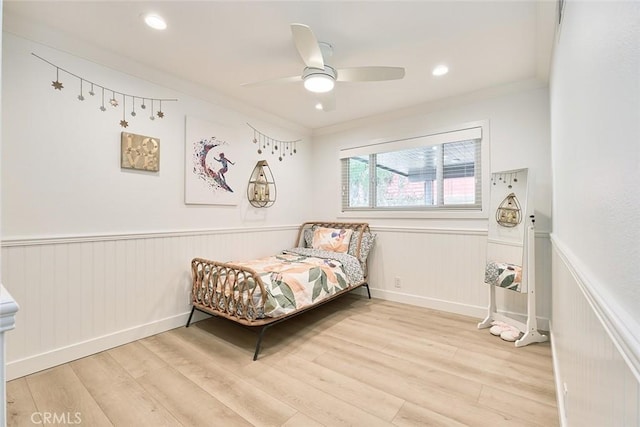 bedroom with a wainscoted wall, ornamental molding, a ceiling fan, and wood finished floors