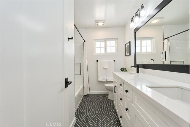 bathroom with double vanity, toilet, baseboards, and a sink