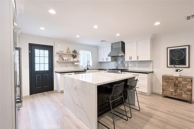 kitchen featuring a kitchen island, light wood-type flooring, wall chimney exhaust hood, and a sink