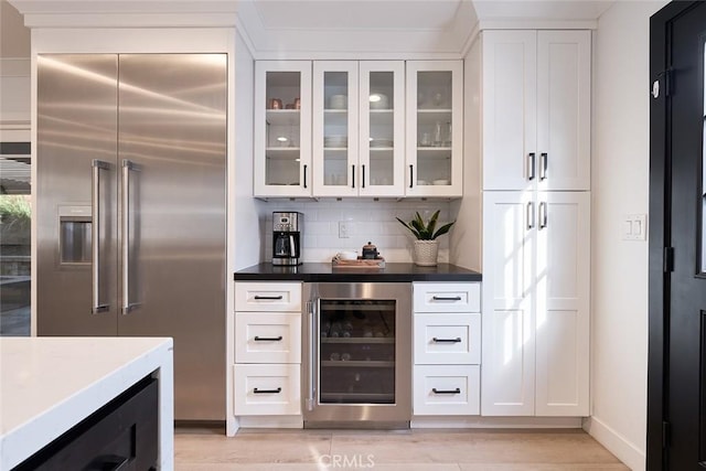 bar with light wood-type flooring, wine cooler, backsplash, and stainless steel built in refrigerator