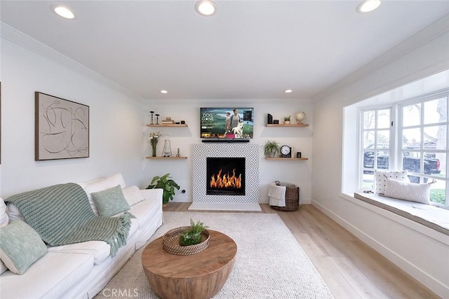 living room featuring recessed lighting, a fireplace, crown molding, and light wood-style floors