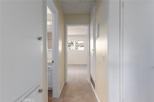 corridor featuring visible vents, light colored carpet, and baseboards