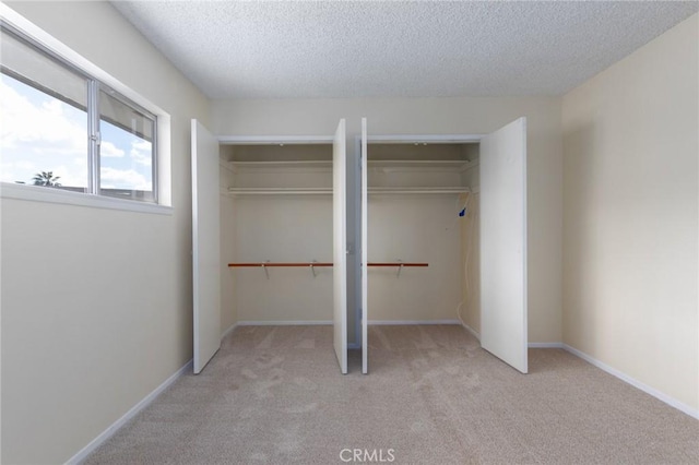 unfurnished bedroom featuring two closets, light carpet, a textured ceiling, and baseboards