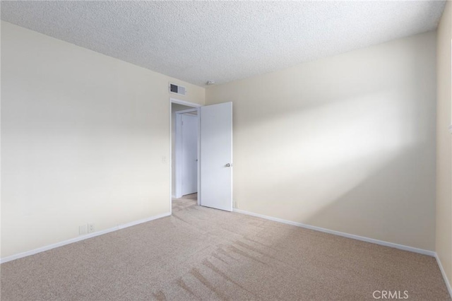 empty room with a textured ceiling, baseboards, visible vents, and light carpet