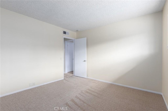 empty room featuring baseboards, visible vents, a textured ceiling, and light colored carpet