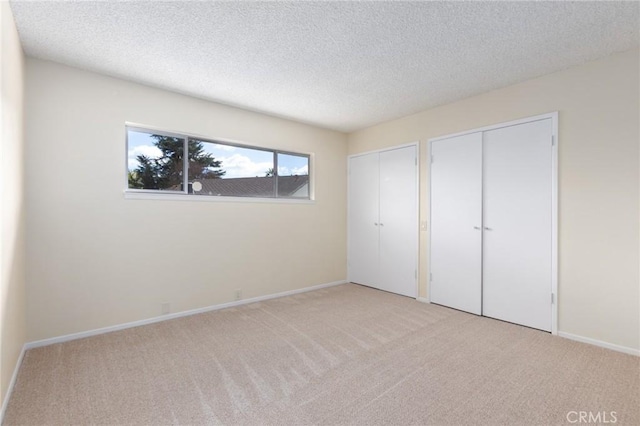 unfurnished bedroom with a textured ceiling, baseboards, two closets, and light carpet