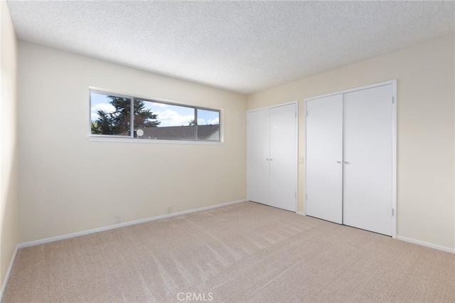 unfurnished bedroom featuring two closets, light carpet, a textured ceiling, and baseboards