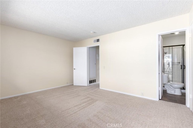 unfurnished bedroom featuring baseboards, carpet floors, a textured ceiling, and ensuite bathroom