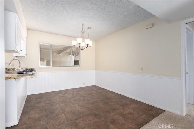 unfurnished dining area featuring a chandelier, a sink, a wainscoted wall, and a textured ceiling