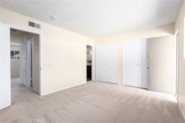 unfurnished bedroom featuring visible vents, carpet floors, a textured ceiling, and multiple closets