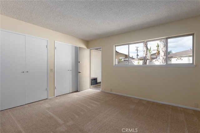 unfurnished bedroom featuring multiple windows, carpet flooring, two closets, and a textured ceiling