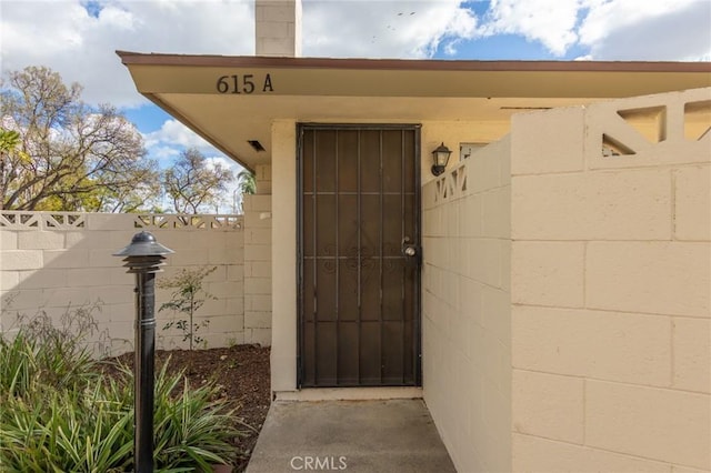 view of exterior entry featuring concrete block siding and fence