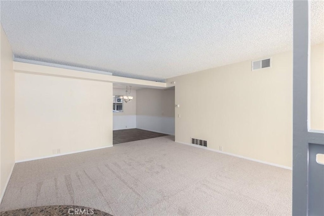 carpeted empty room with a notable chandelier, baseboards, visible vents, and a textured ceiling