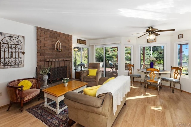 living area featuring a brick fireplace, a ceiling fan, baseboards, and light wood finished floors