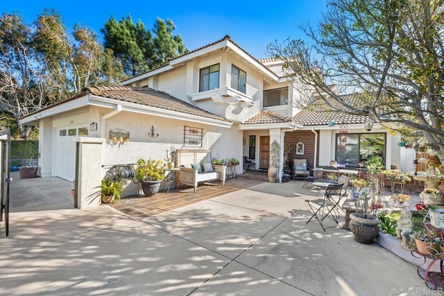 rear view of house with a patio, an attached garage, stucco siding, concrete driveway, and a tiled roof