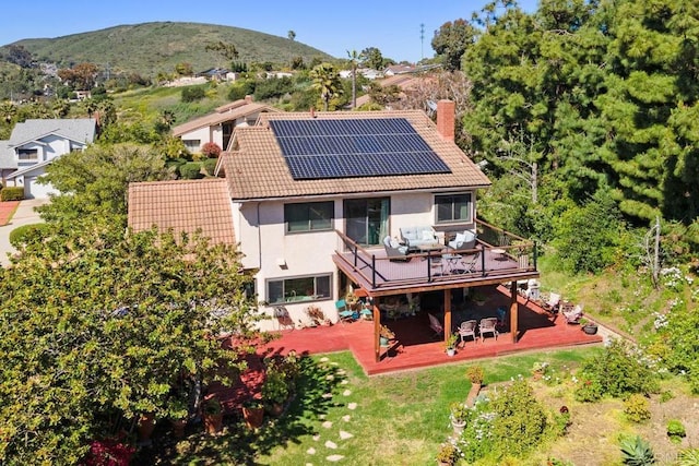 back of property featuring a deck with mountain view, a tile roof, a patio, roof mounted solar panels, and a chimney