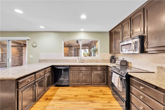 kitchen with light wood finished floors, a peninsula, a sink, black appliances, and dark brown cabinetry