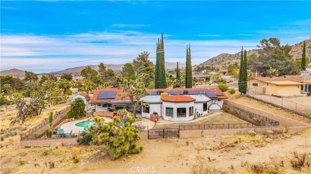 back of property with a fenced front yard, solar panels, a mountain view, and a gate