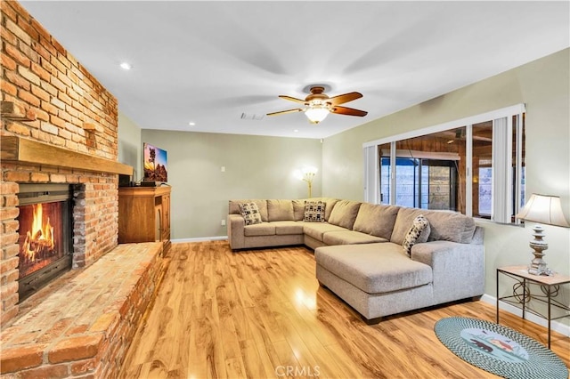 living area featuring visible vents, a brick fireplace, baseboards, wood finished floors, and a ceiling fan