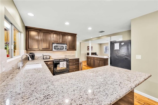 kitchen featuring light stone counters, visible vents, a peninsula, a sink, and black appliances