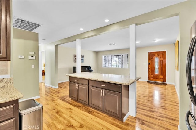 kitchen with stainless steel fridge, light wood-style flooring, light stone countertops, and visible vents