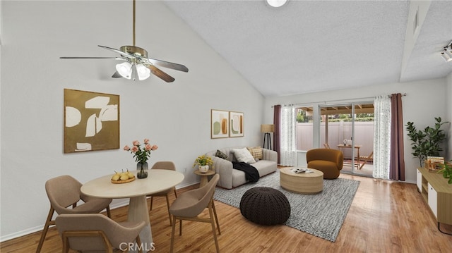 living room with baseboards, light wood-style flooring, a textured ceiling, high vaulted ceiling, and a ceiling fan