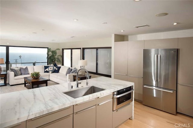 kitchen featuring visible vents, a sink, light stone counters, stainless steel appliances, and light wood-style floors