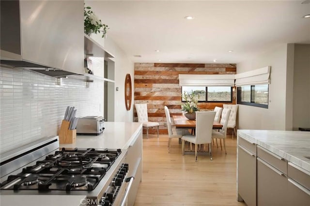 kitchen with light wood finished floors, gray cabinetry, light countertops, decorative backsplash, and gas stove