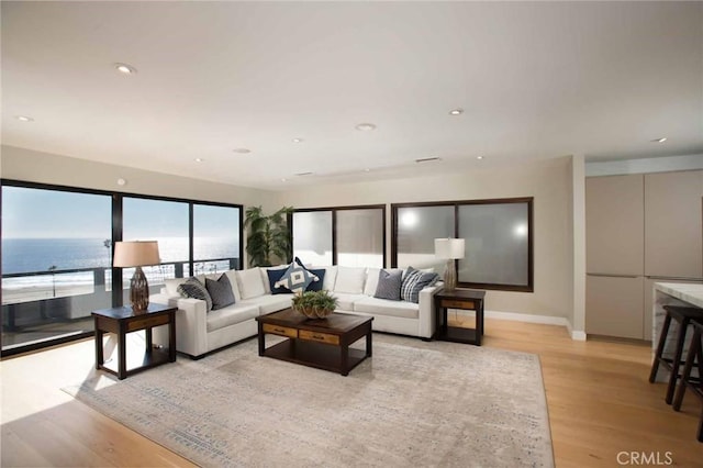 living room with recessed lighting, a water view, light wood finished floors, and baseboards