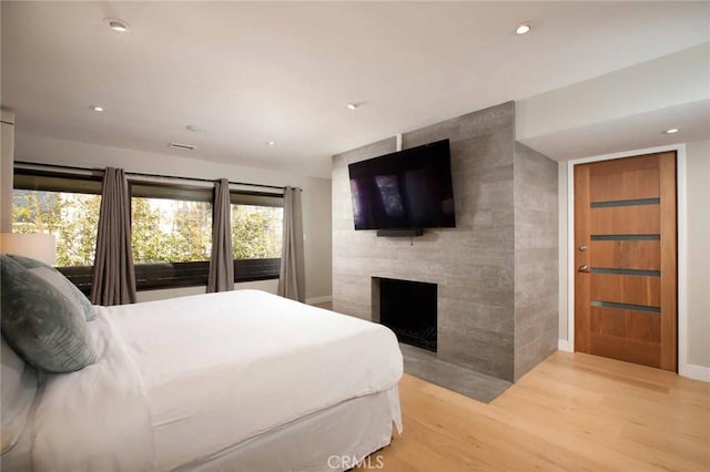 bedroom with recessed lighting, wood finished floors, and a tile fireplace